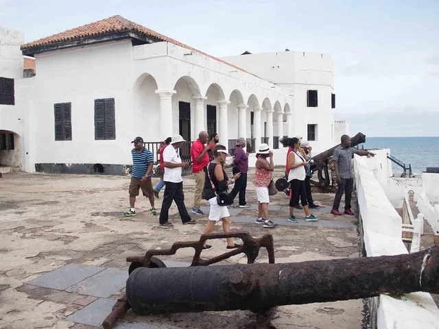 Group of tourists walking along the upper level of a white coastal fort.
