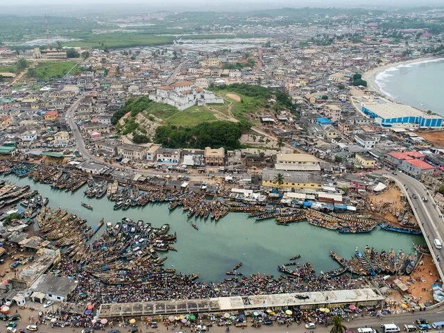 Aerial view of a coastal city with a prominent white fort and crowded harbor.