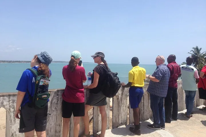 Turistas de pie junto a un muro blanco mirando hacia el océano.