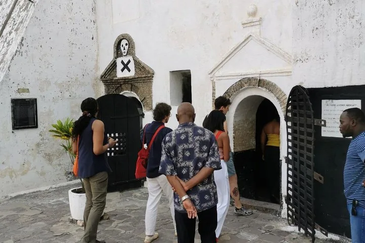 Touristen versammeln sich in der Nähe eines bogenförmigen Eingangs eines weißen Steingebäudes mit einem Totenkopf-Emblem.